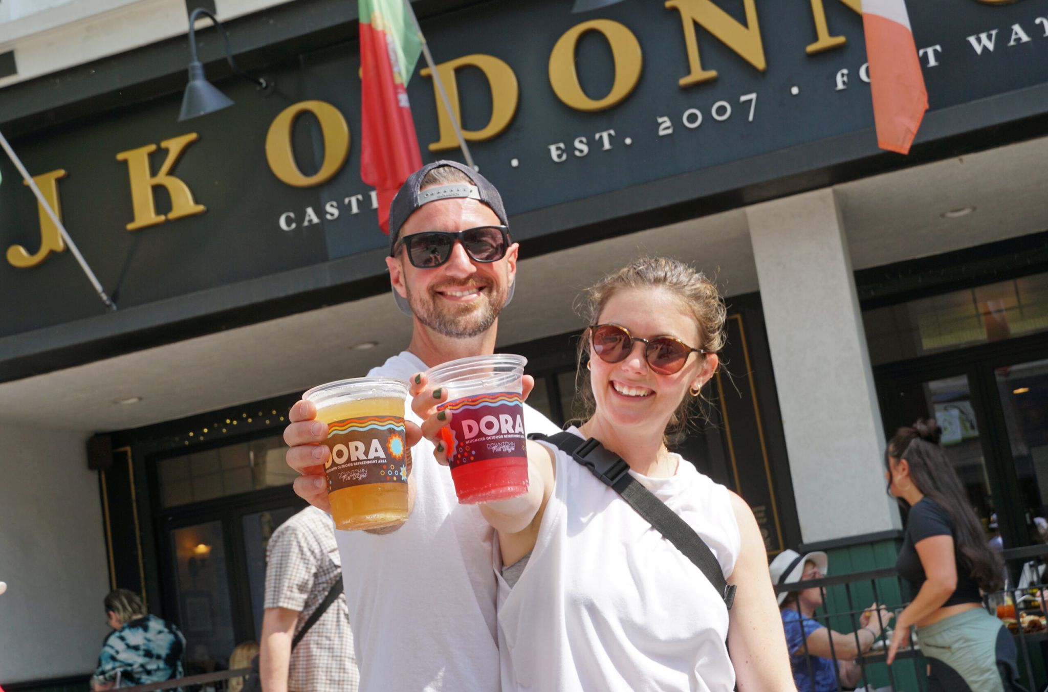 A couple posing with DORA cups outside of a bar